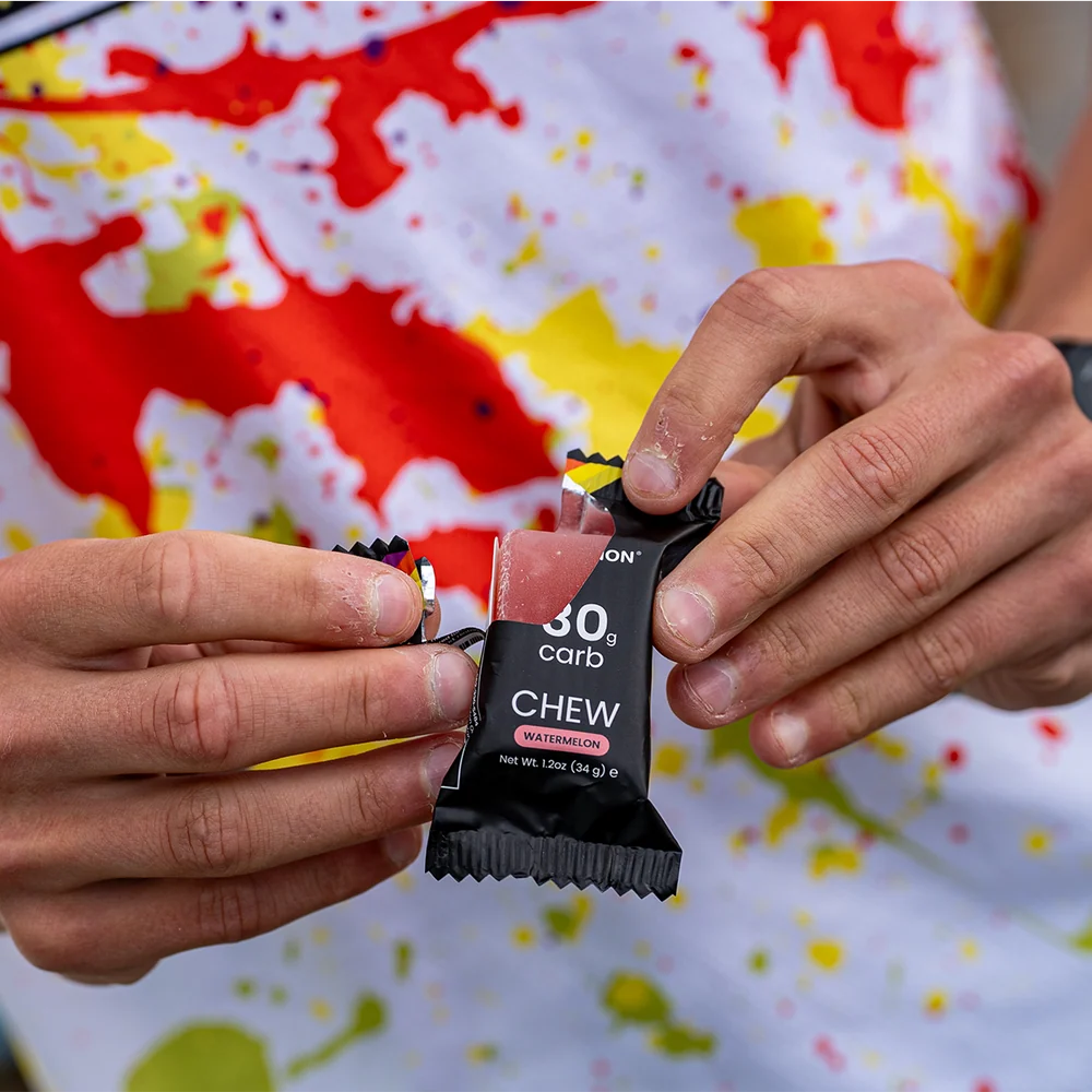 Person holding a black snack package with '30g carb' text against a colorful background