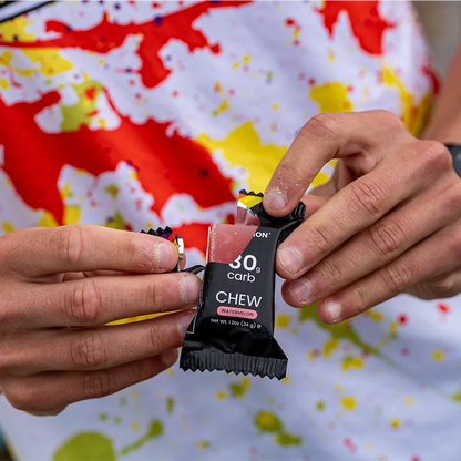 Person holding a black snack package with '30g carb' text against a colorful background