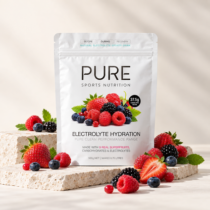 A stand-up pouch of PURE Sports Nutrition Electrolyte Hydration drink mix, surrounded by fresh strawberries, blueberries, raspberries, and blackberries on a light stone surface against a warm off-white background.